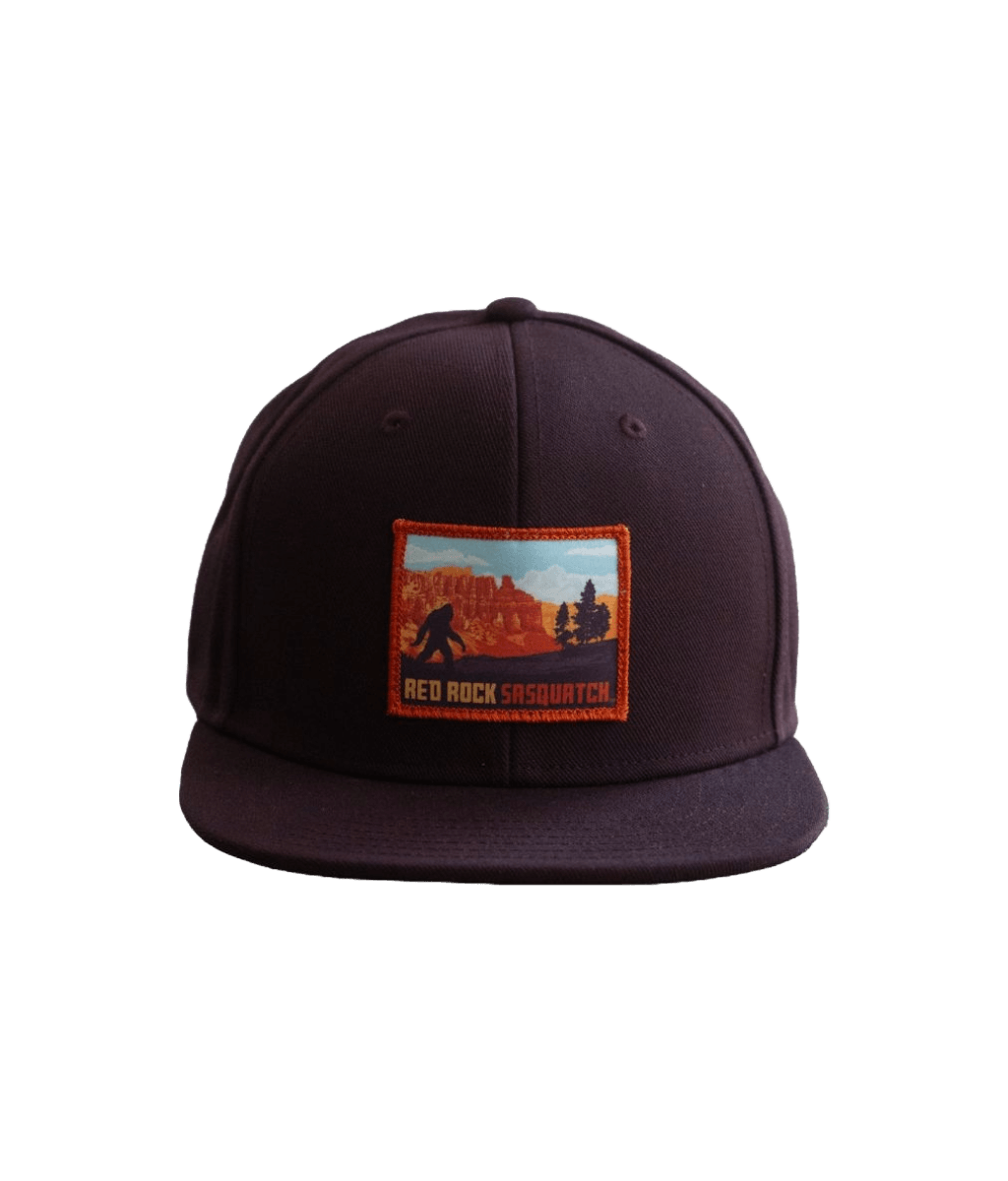 Bryce Canyon flat brim hat. Features a patch with a Sasquatch silhouette in a Bryce Canyon National Park landscape on a dark-colored flat brim hat.